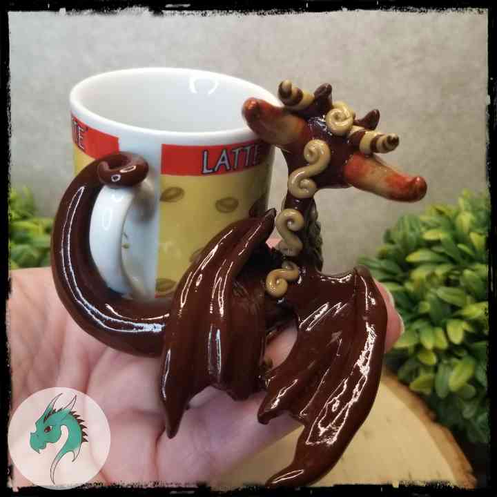 Back view of a clay dragon leaning on a ceramic mug