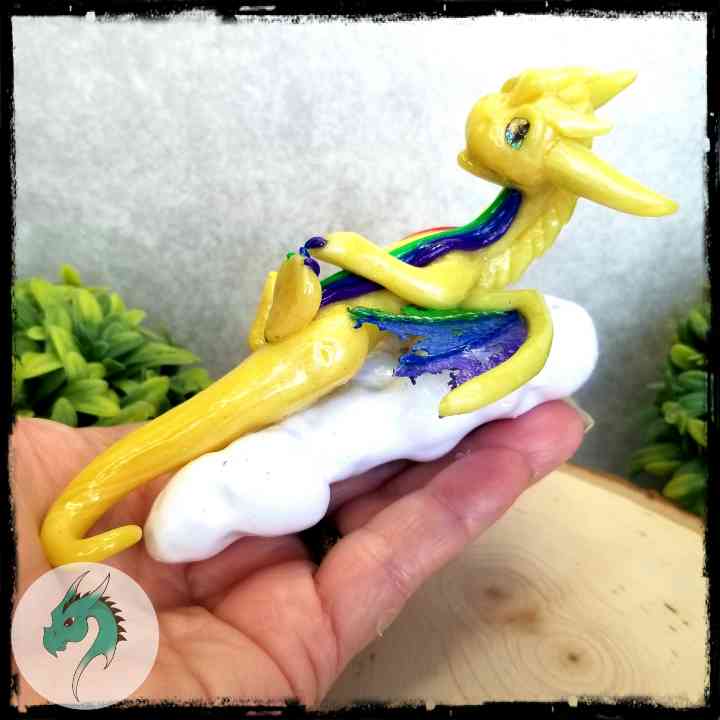 Hand holding a yellow dragon with rainbow colors resting on a cloud