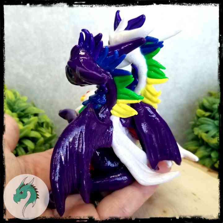 Back view of a hand holding a pair of clay dragons with rainbow accents