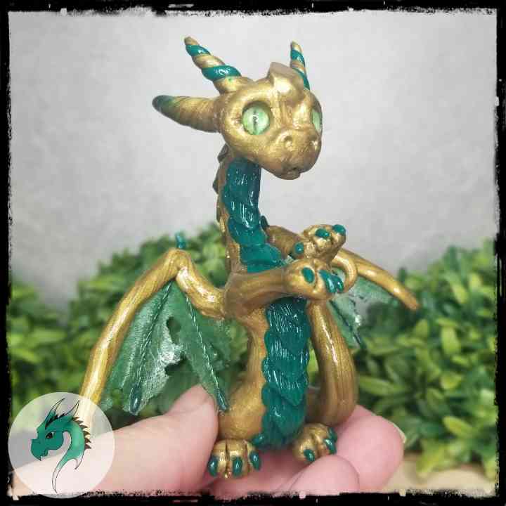 Hand holding a gold and green clay dragon against a leafy background