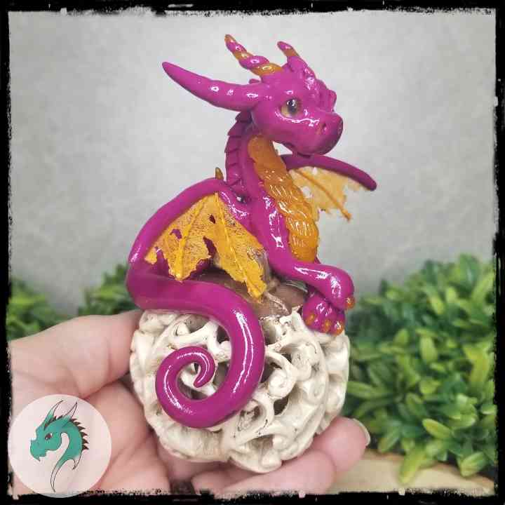 Hand holding a fuchsia clay dragon on a white resin pumpkin