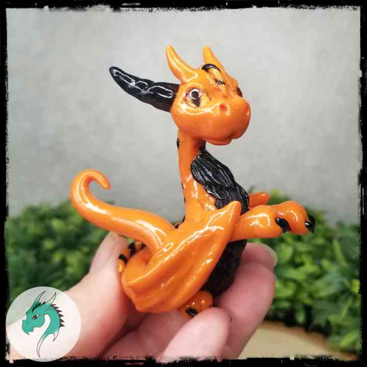 Hand holding a clay orange and black dragon