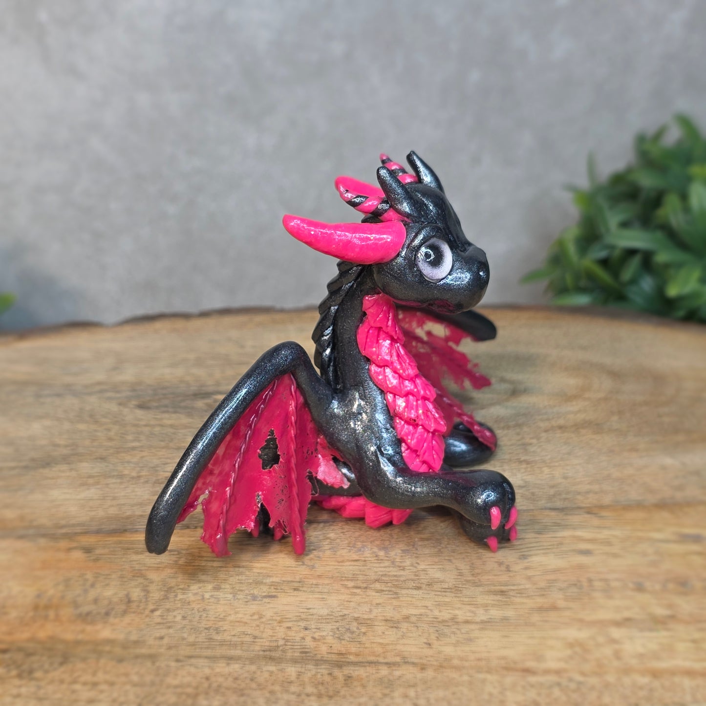 A graphite and pink clay dragon against a blurred wood surface