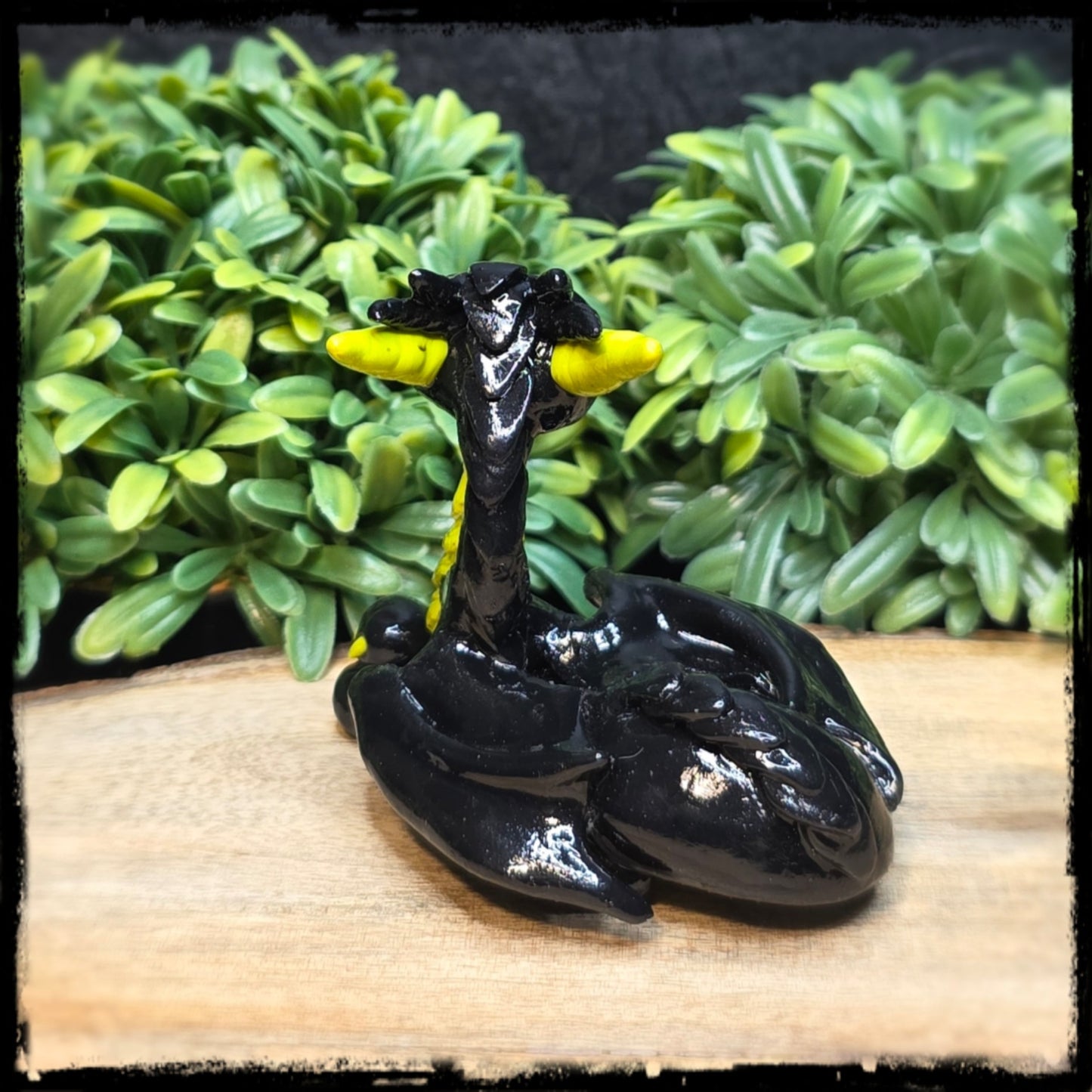 Black dragon figurine with yellow wings on a wooden surface with green foliage in the background