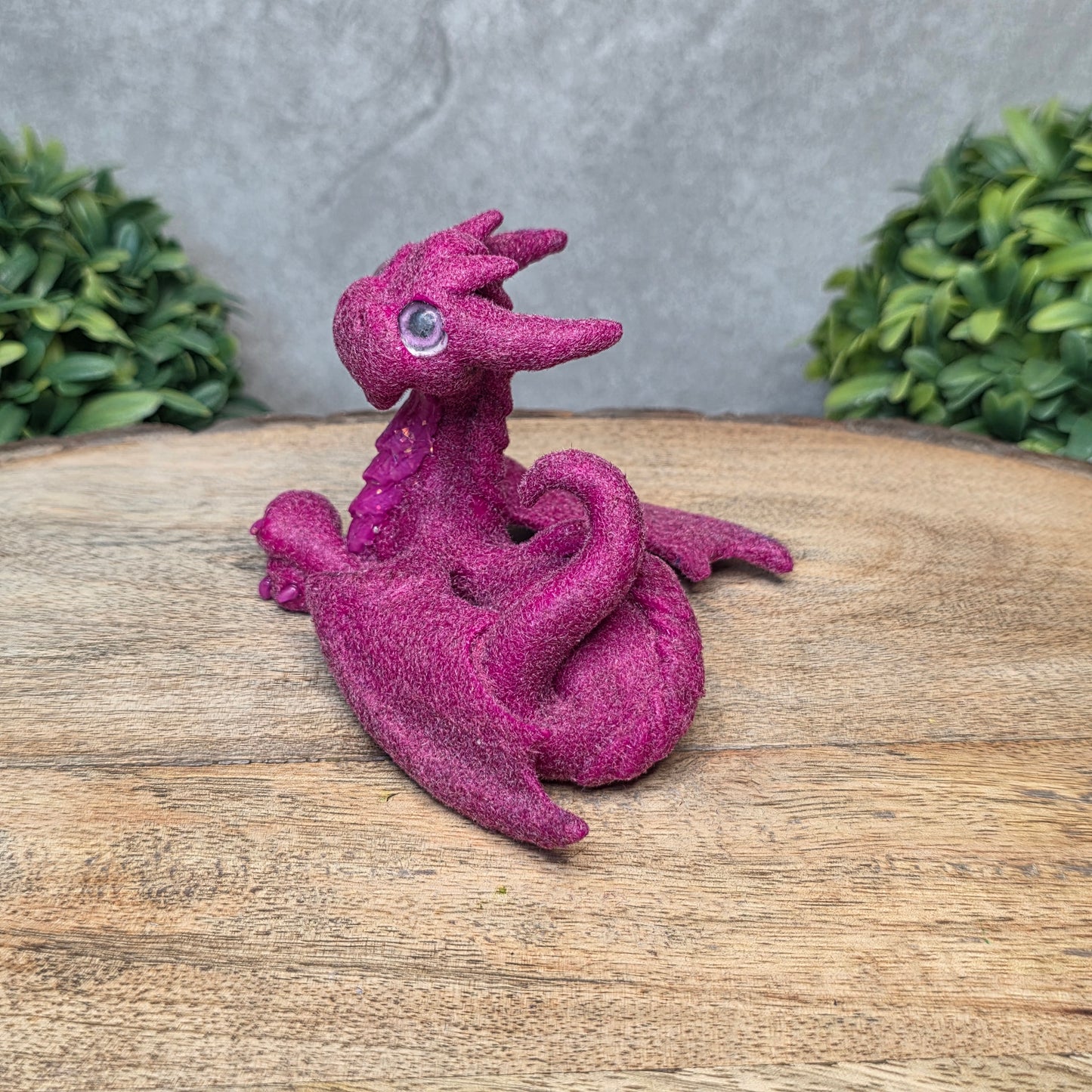 A flocked clay dragon sculpture on a wood surface with greenery.