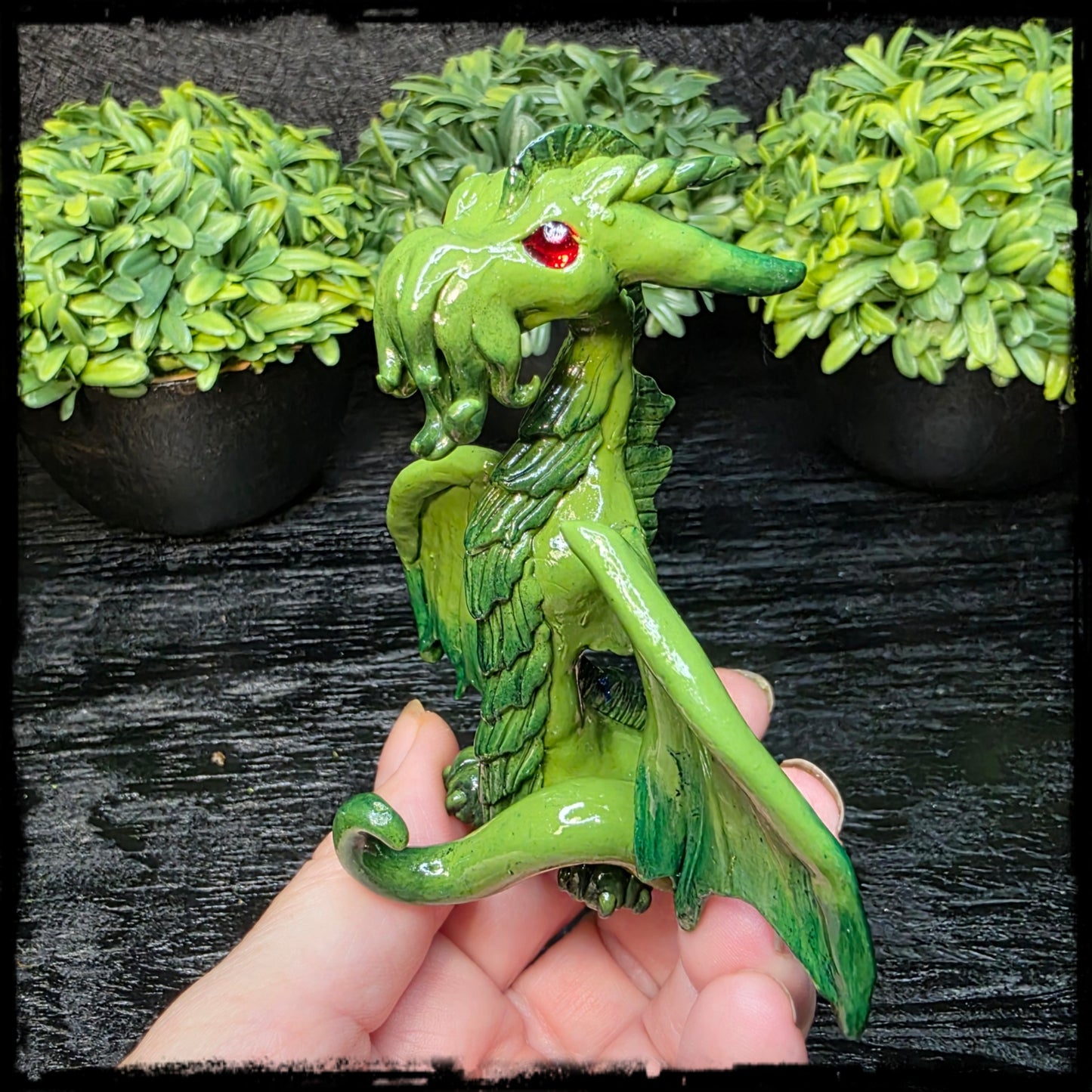Green dragon figurine held in a hand with decorative green foliage in the background
