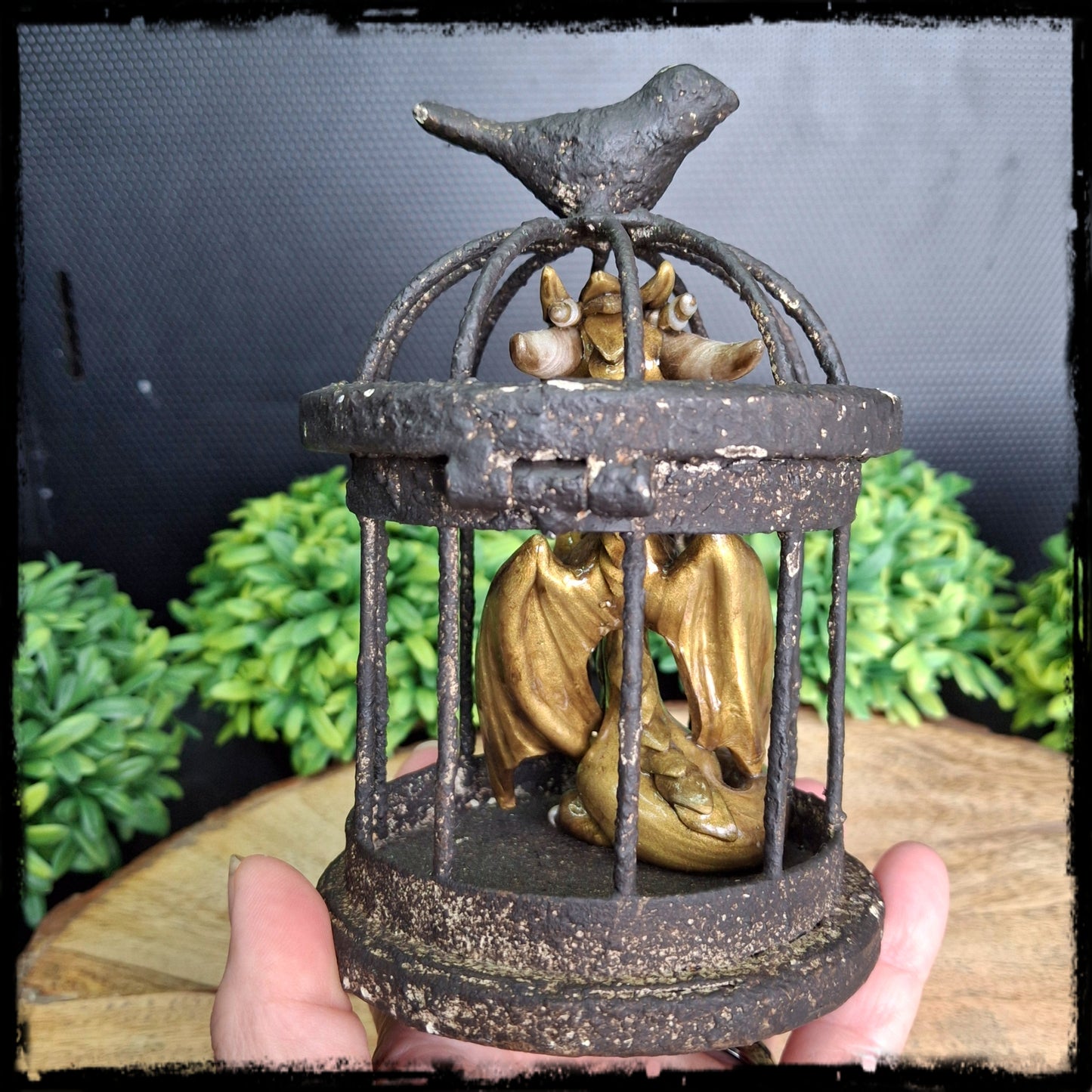 Hand holding a clay dragon inside a rusty cage