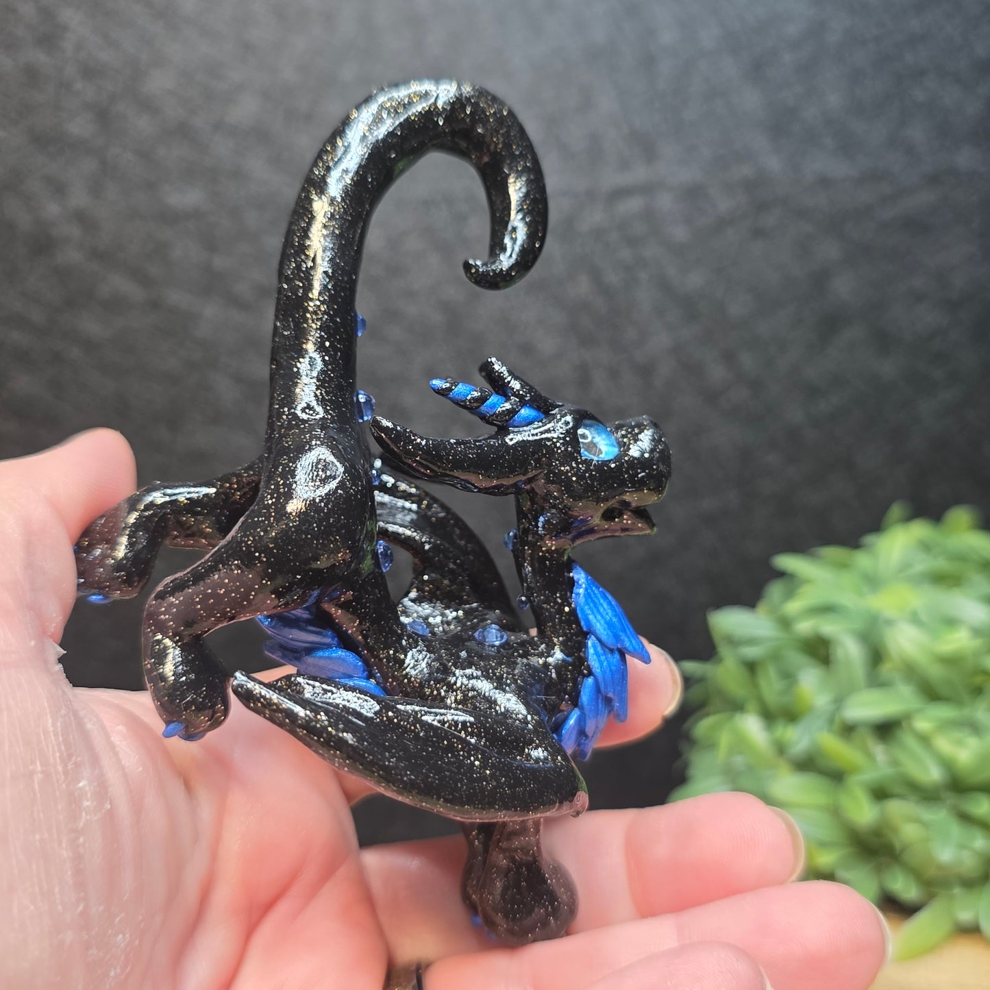 Hand holding a black and blue clay dragon