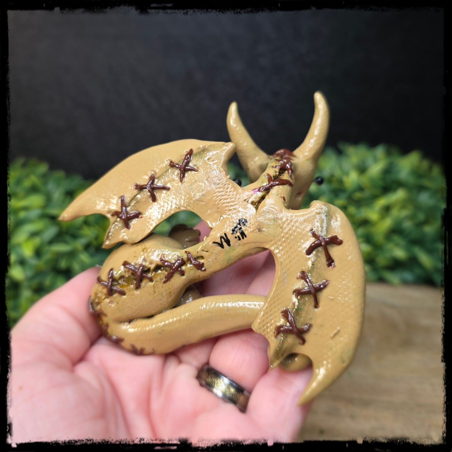 Back view of a hand holding a clay voodoo dragon with dark stitching