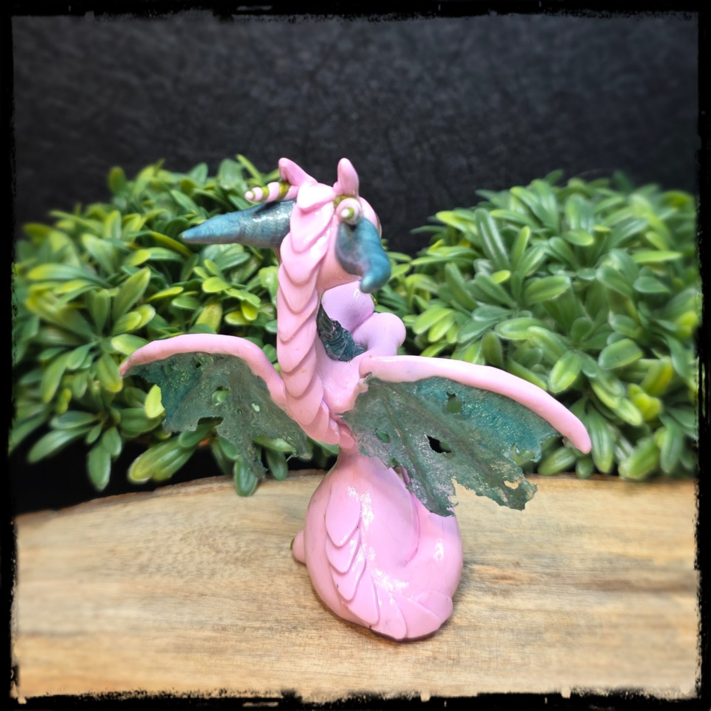 Pink dragon figurine on a wooden surface with green foliage in the background