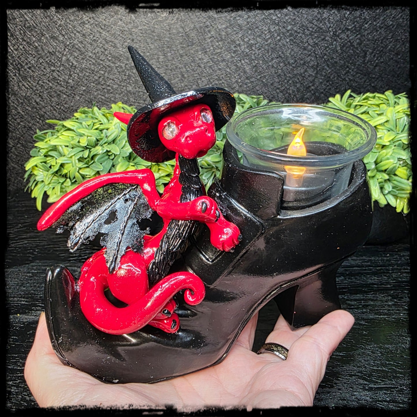 Witch boot with red and black clay dragon holding a candle against a dark background