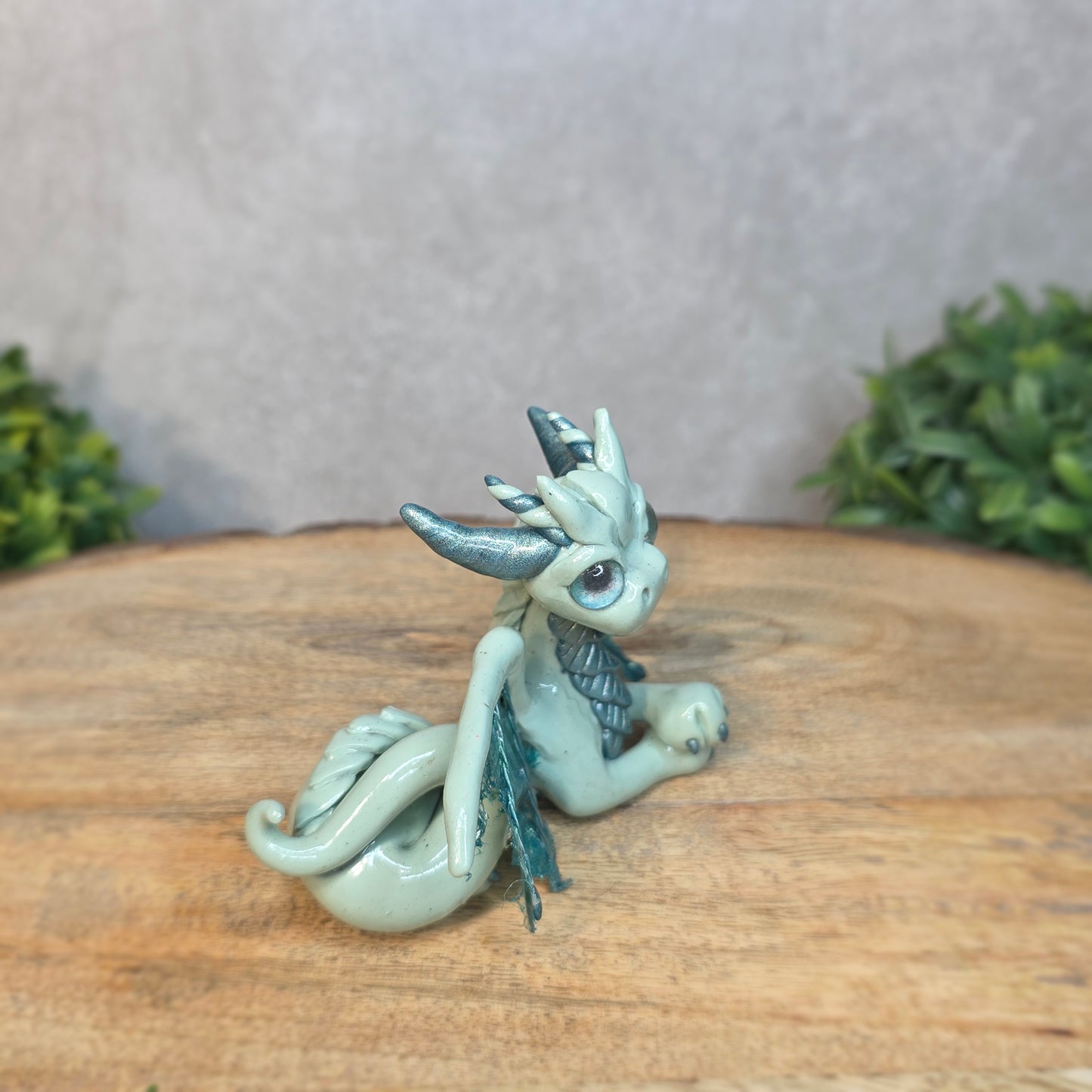 An aqua and turquoise clay dragon against a blurred wood surface