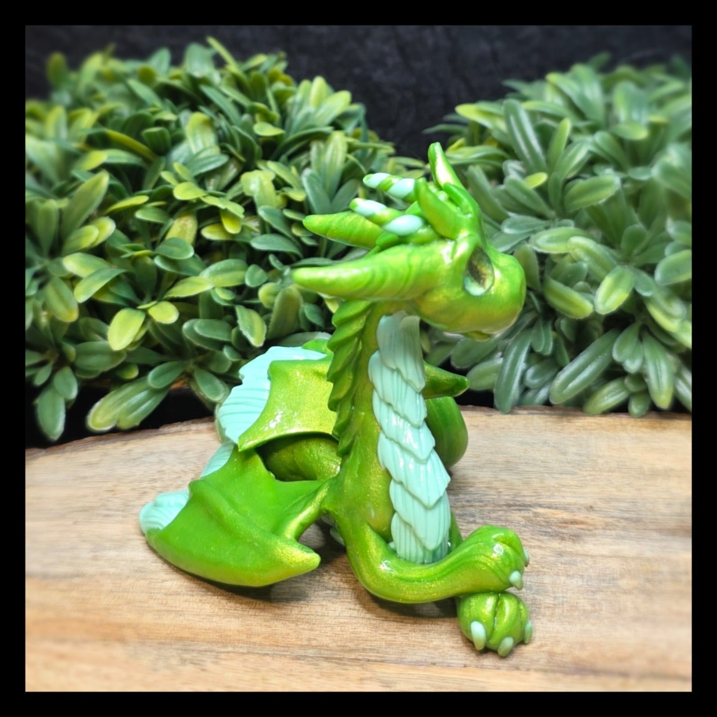 Green dragon figurine on a wooden surface with green foliage in the background