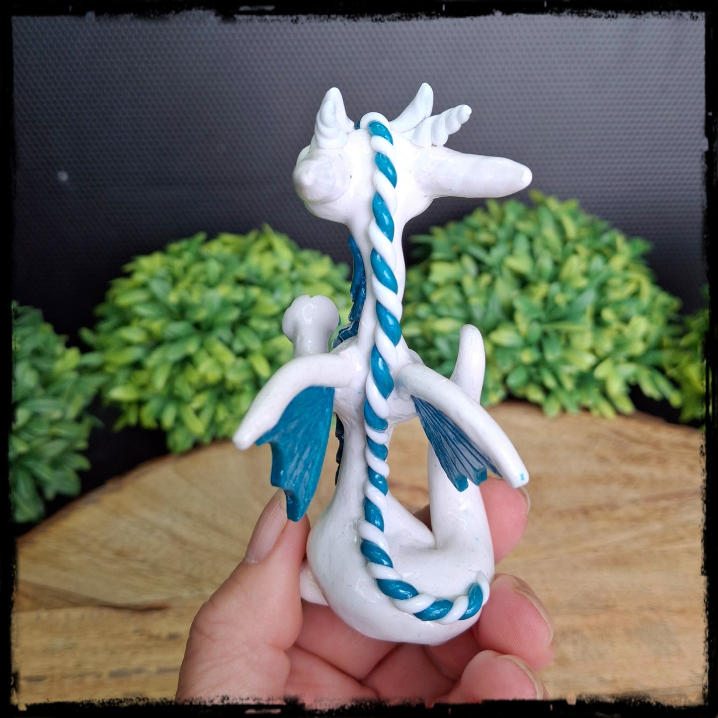White and blue dragon figurine held in hand with a blurred natural background