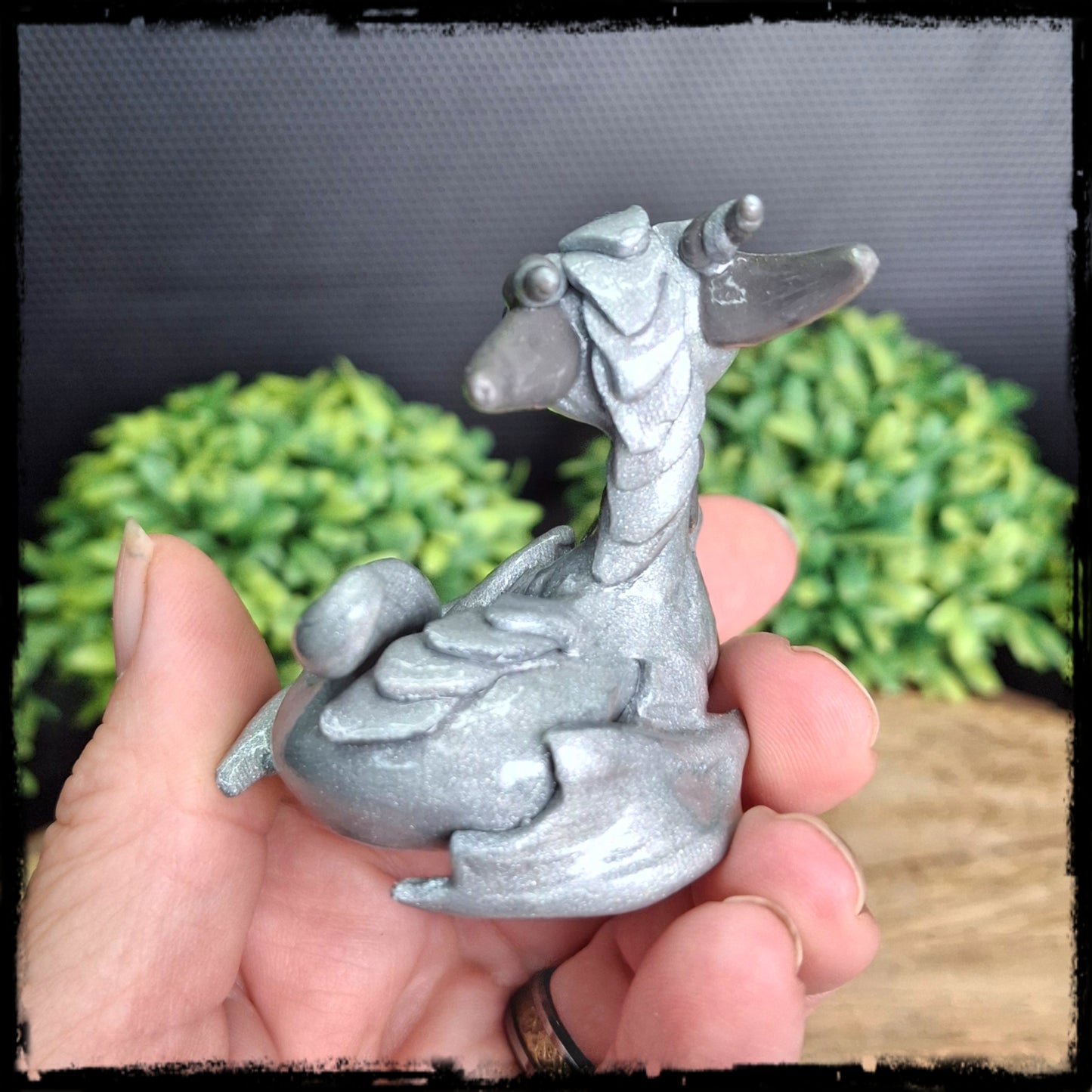 Small silver dragon figurine held in a hand with a blurred natural background.