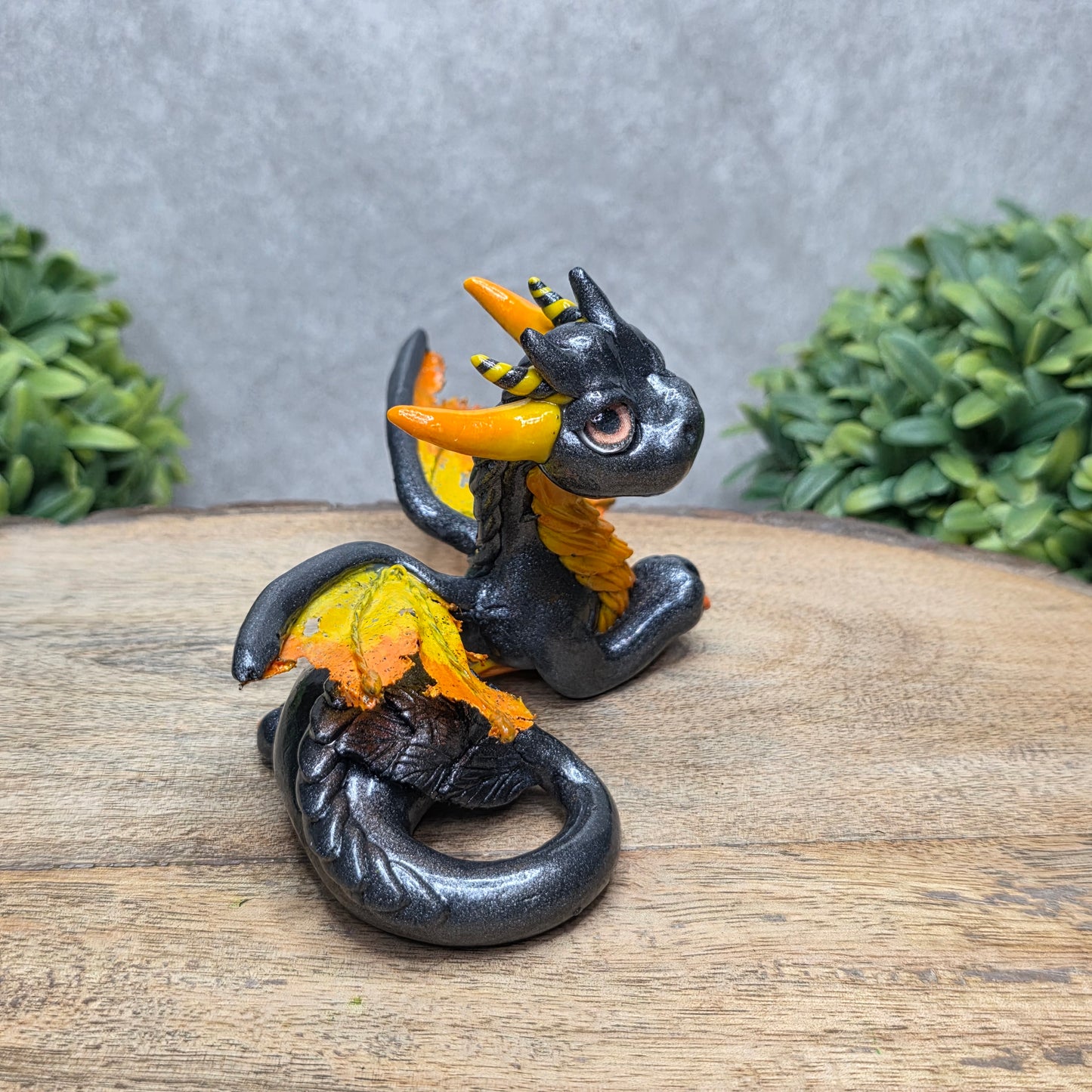 Side view of a clay dragon against a wood surface with greenery.