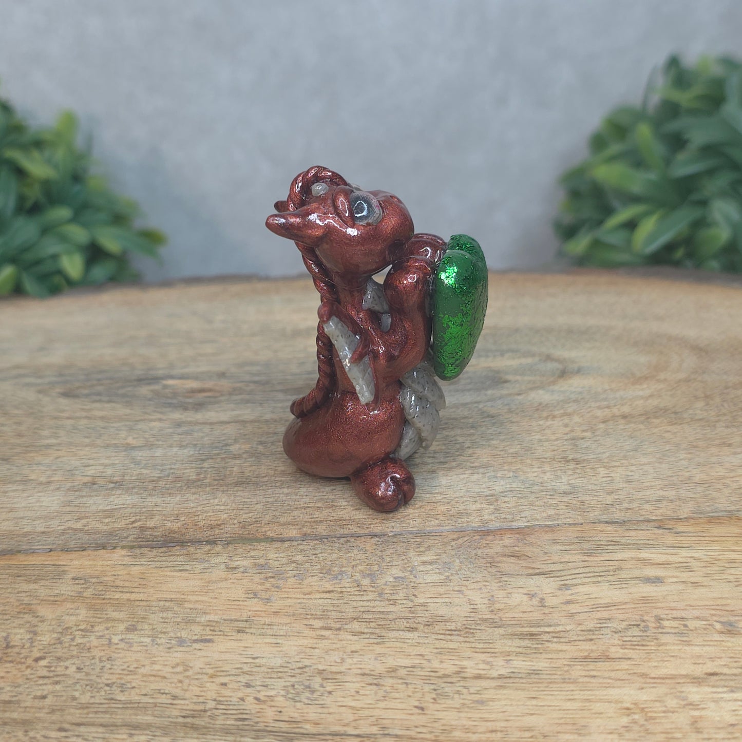 A baby polymer clay dragon with a green heart against a blurred background