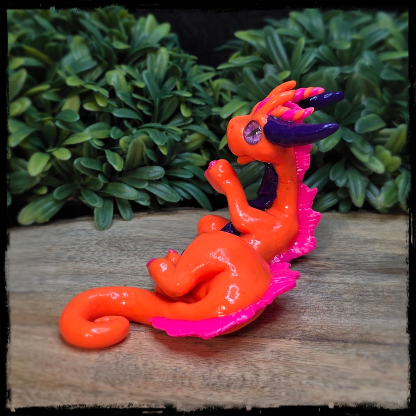 Colorful dragon figurine on a wooden surface with green foliage in the background