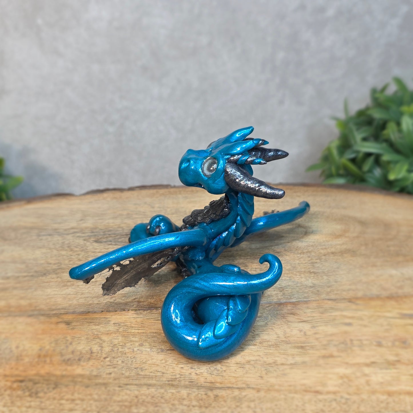 A blue and graphite clay dragon against a blurred wood surface