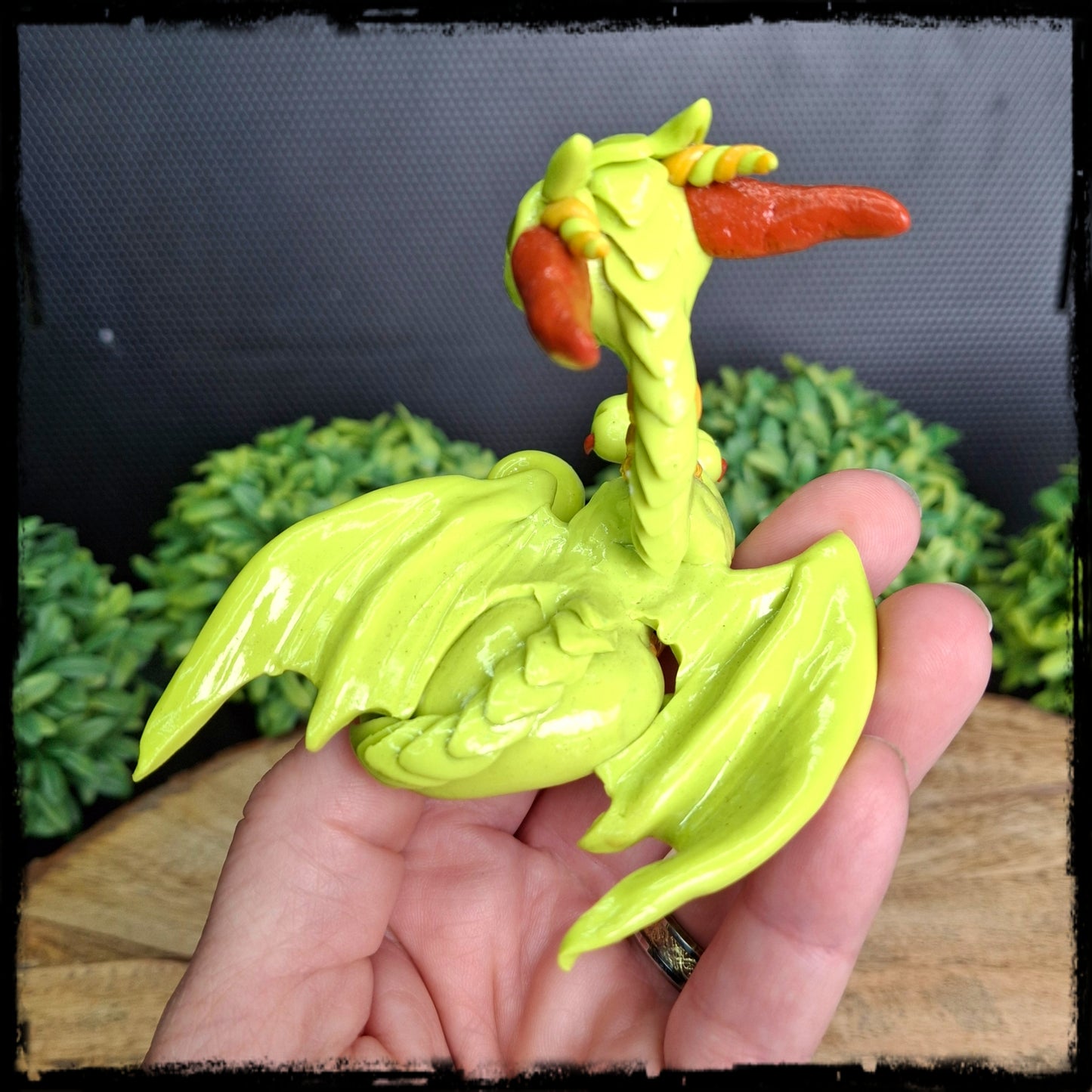 Back view of a hand holding a yellow green clay dragon with orange accents