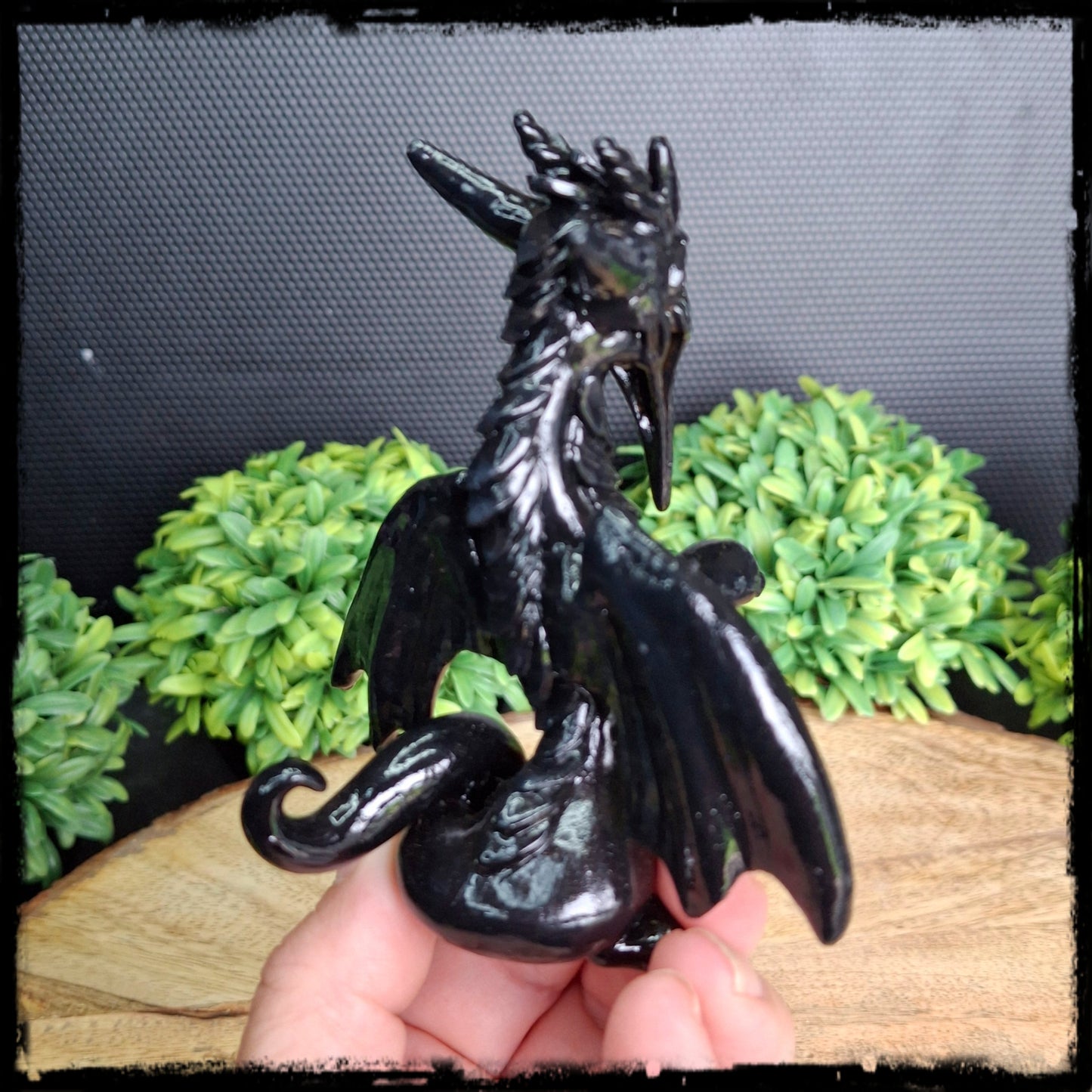 Black dragon figurine held in hand with greenery in the background