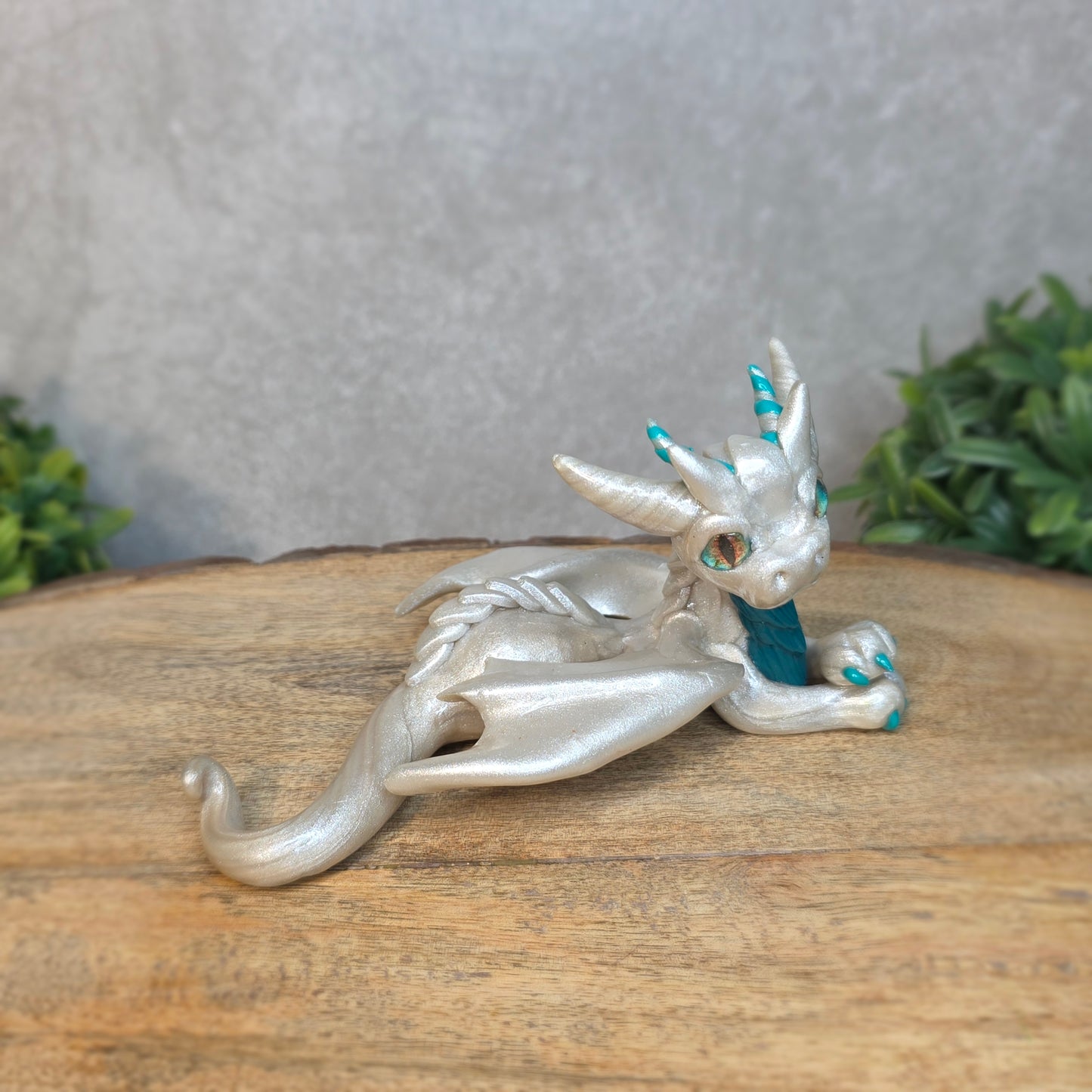 A white and teal clay dragon against a blurred wood surface