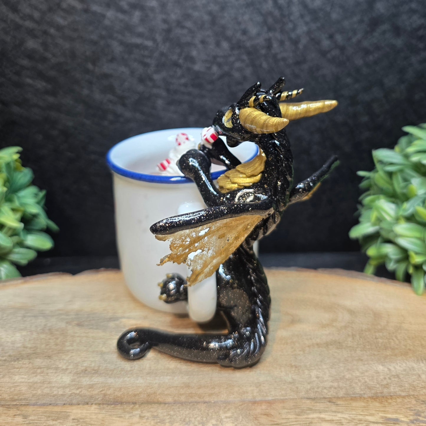 Decorative dragon figurine holding a small cup with candy canes on a wooden surface.