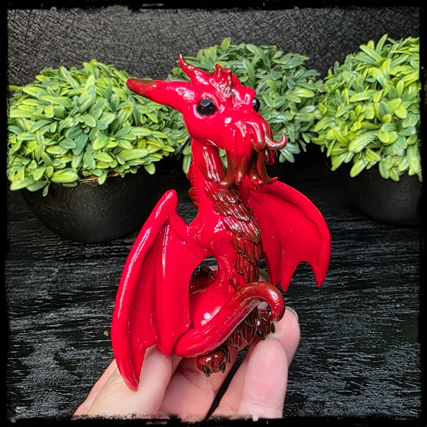 Red Cthulhu dragon figurine held by a hand with green plants in the background