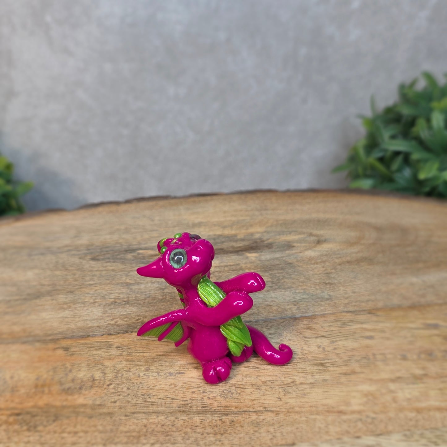 A pink and green clay dragon with a blurred background