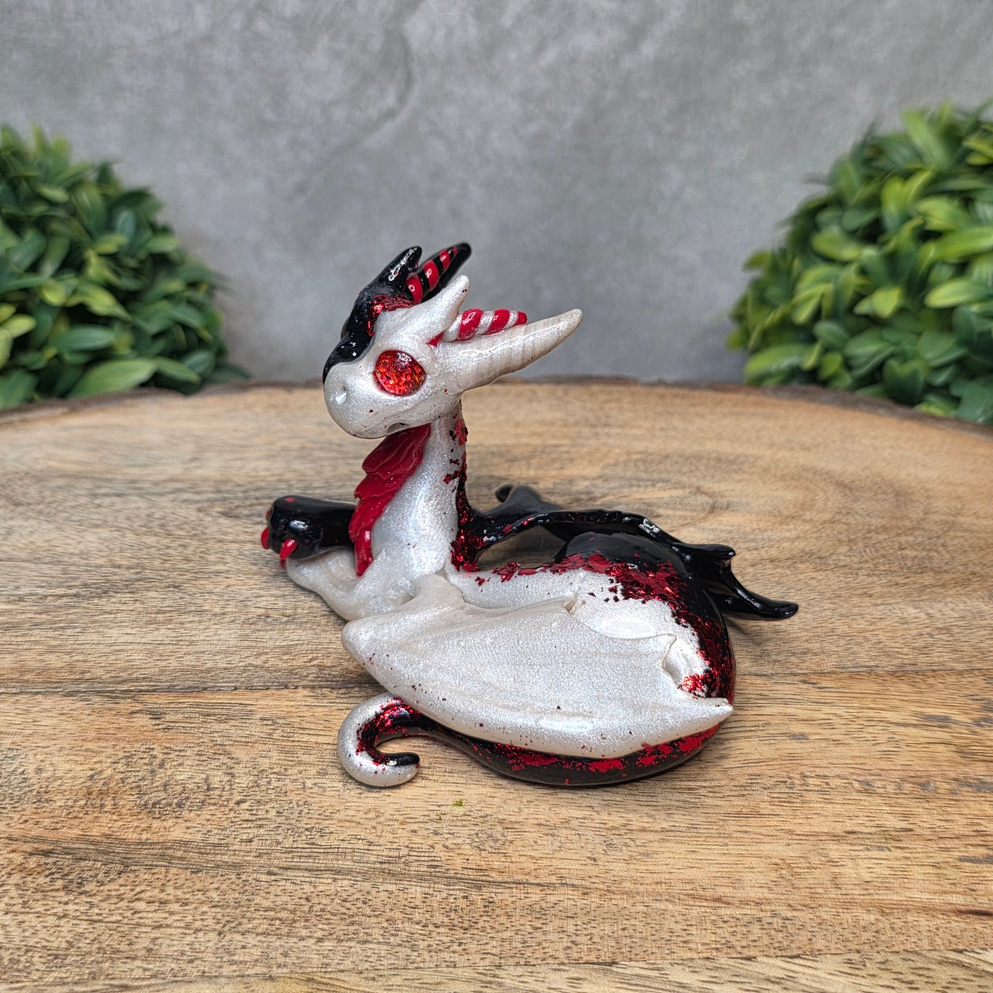 A 2 toned clay dragon sculpture on a wood surface with greenery.