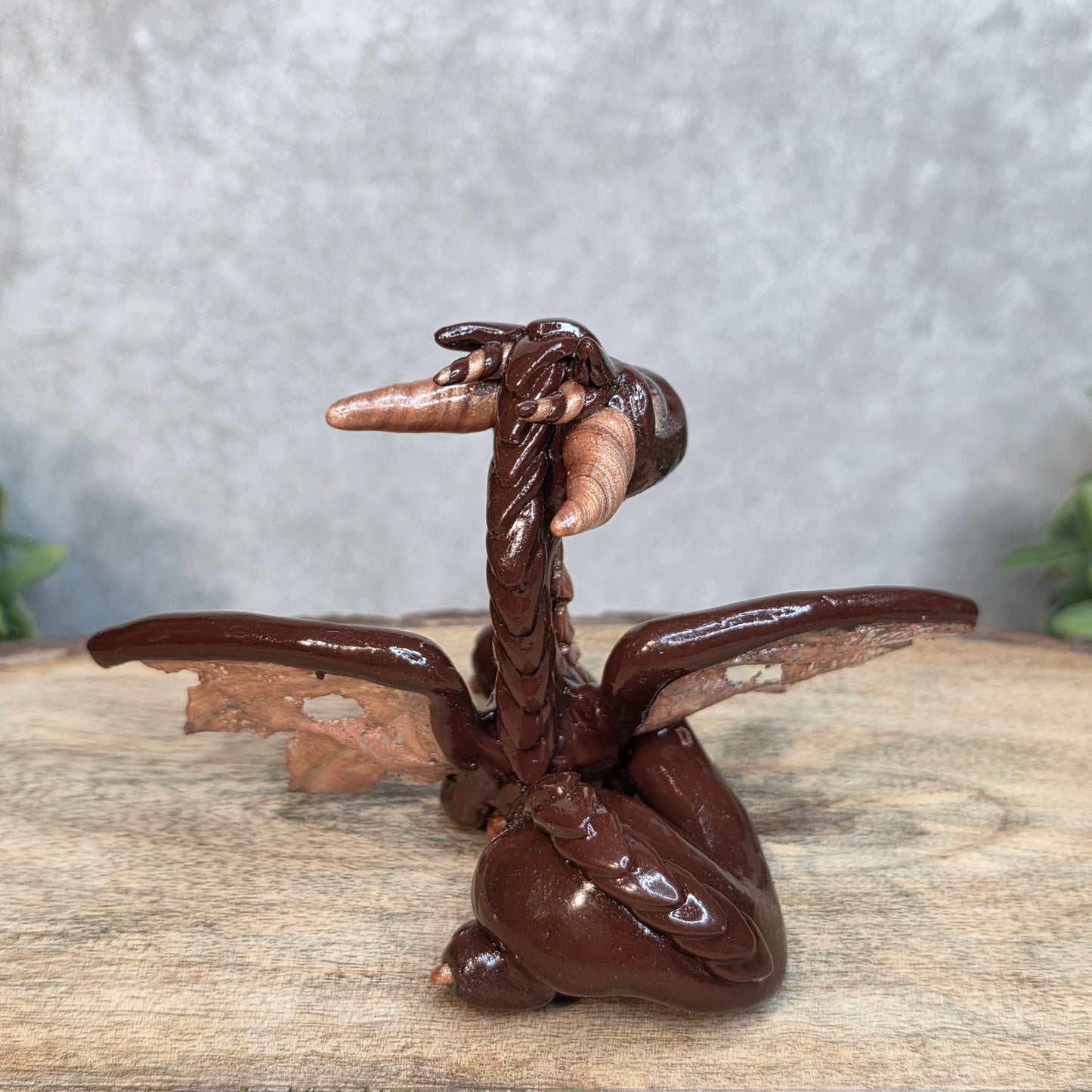 A brown and copper clay dragon against a blurred wood surface