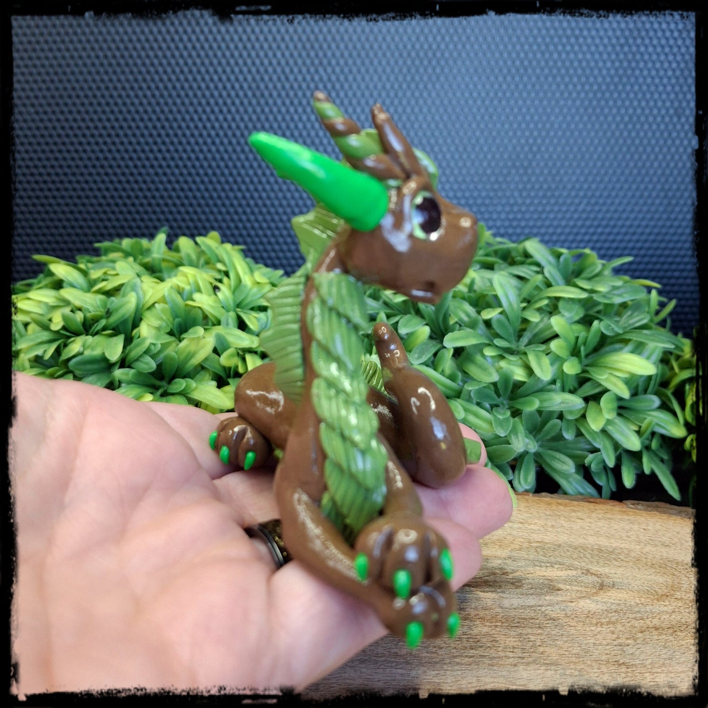 Hand holding a brown and green clay dragon against a leafy background