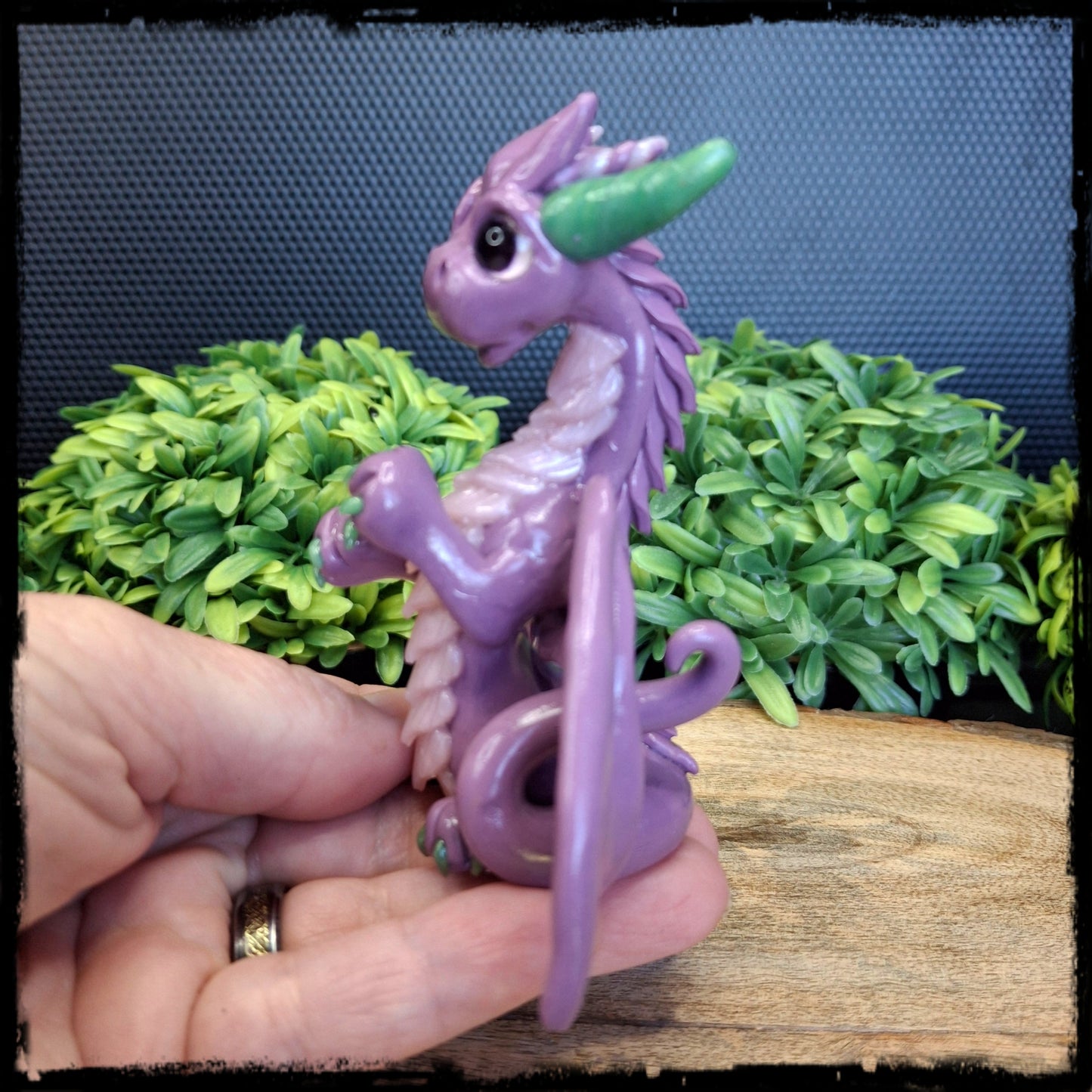 Hand holding a purple clay dragon against a leafy background