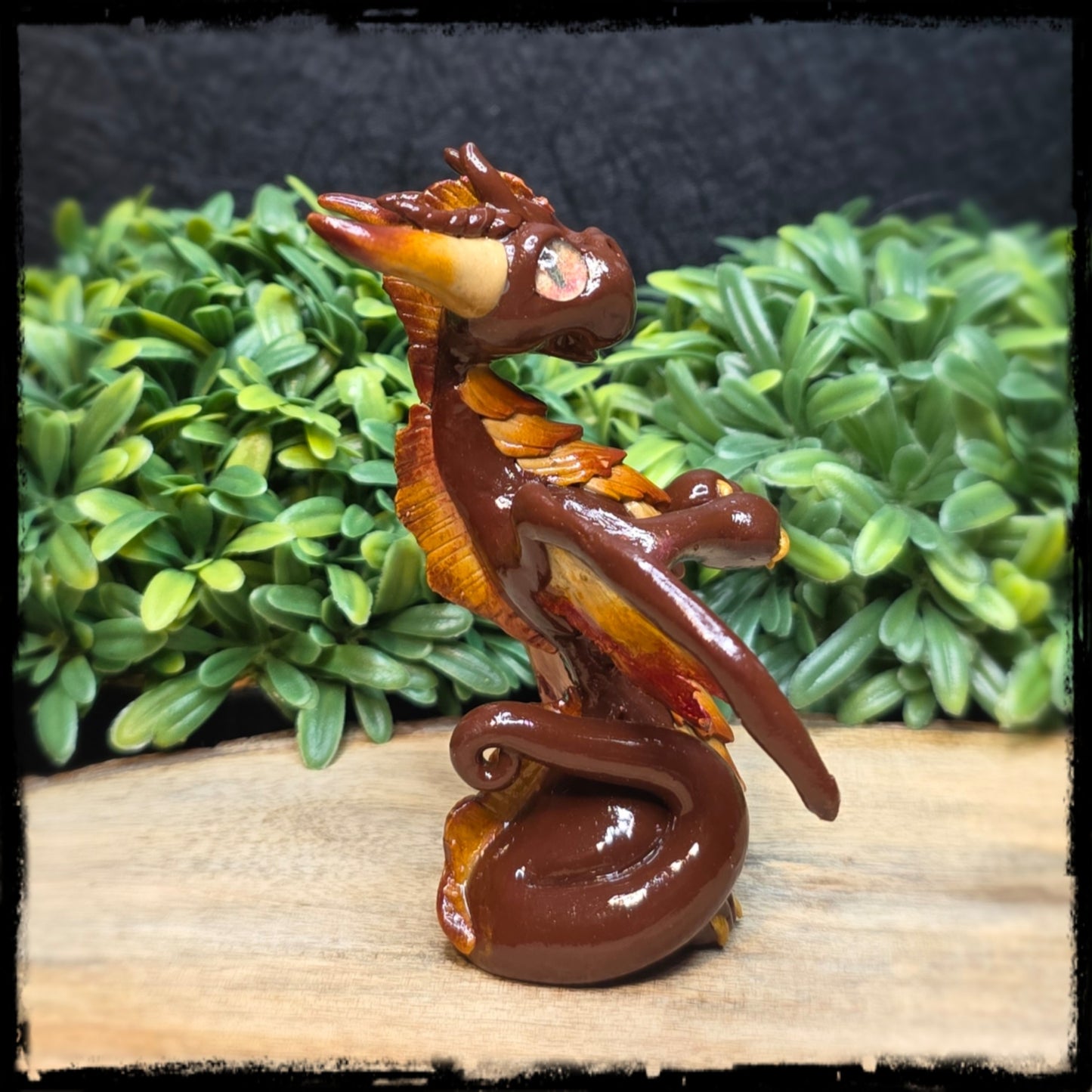 Clay dragon figurine on a wooden surface with green foliage in the background