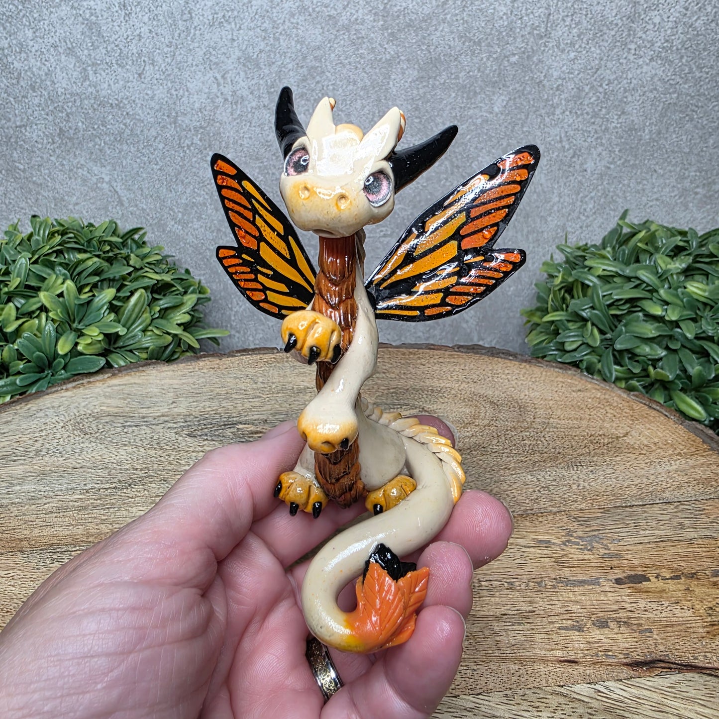 A hand holding a clay dragon with butterfly wings