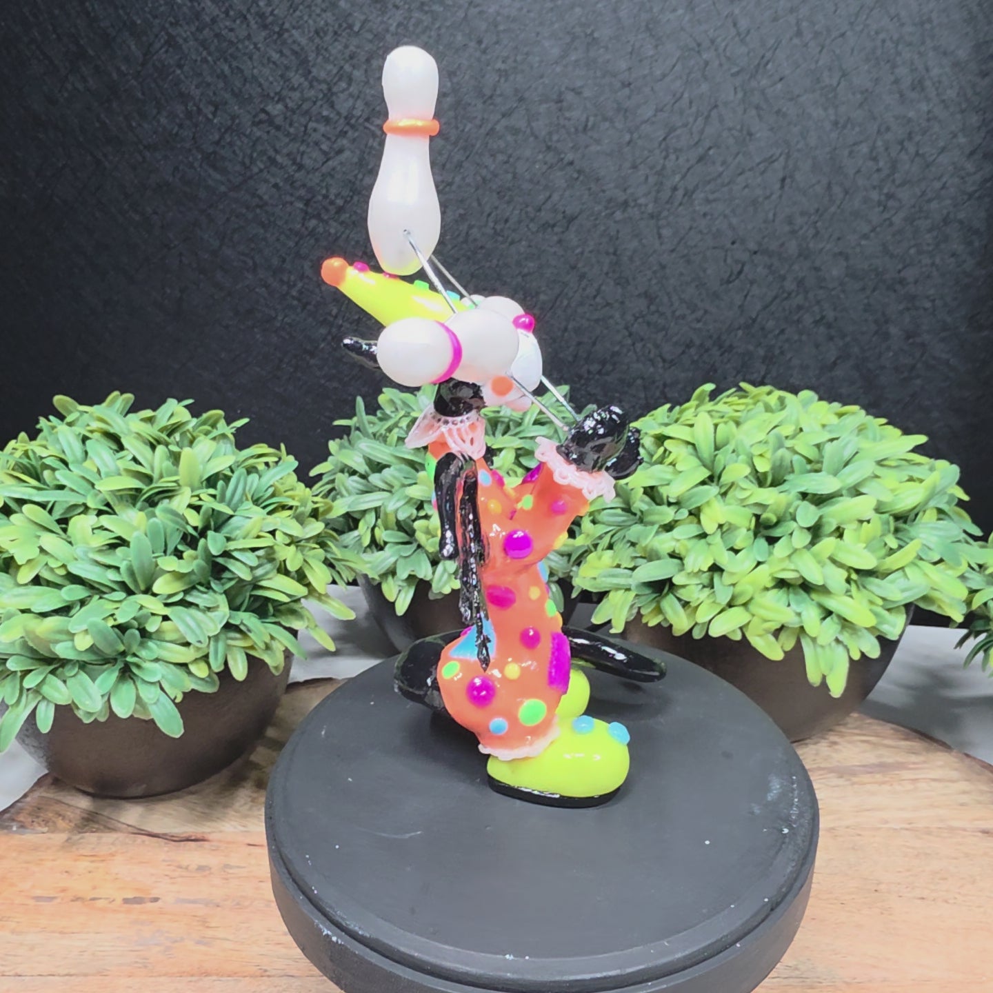 A video of a clown dragon juggling on a wood surface with greenery