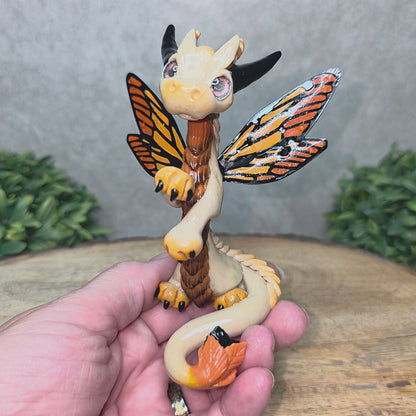A video of a hand holding a clay dragon with butterfly wings