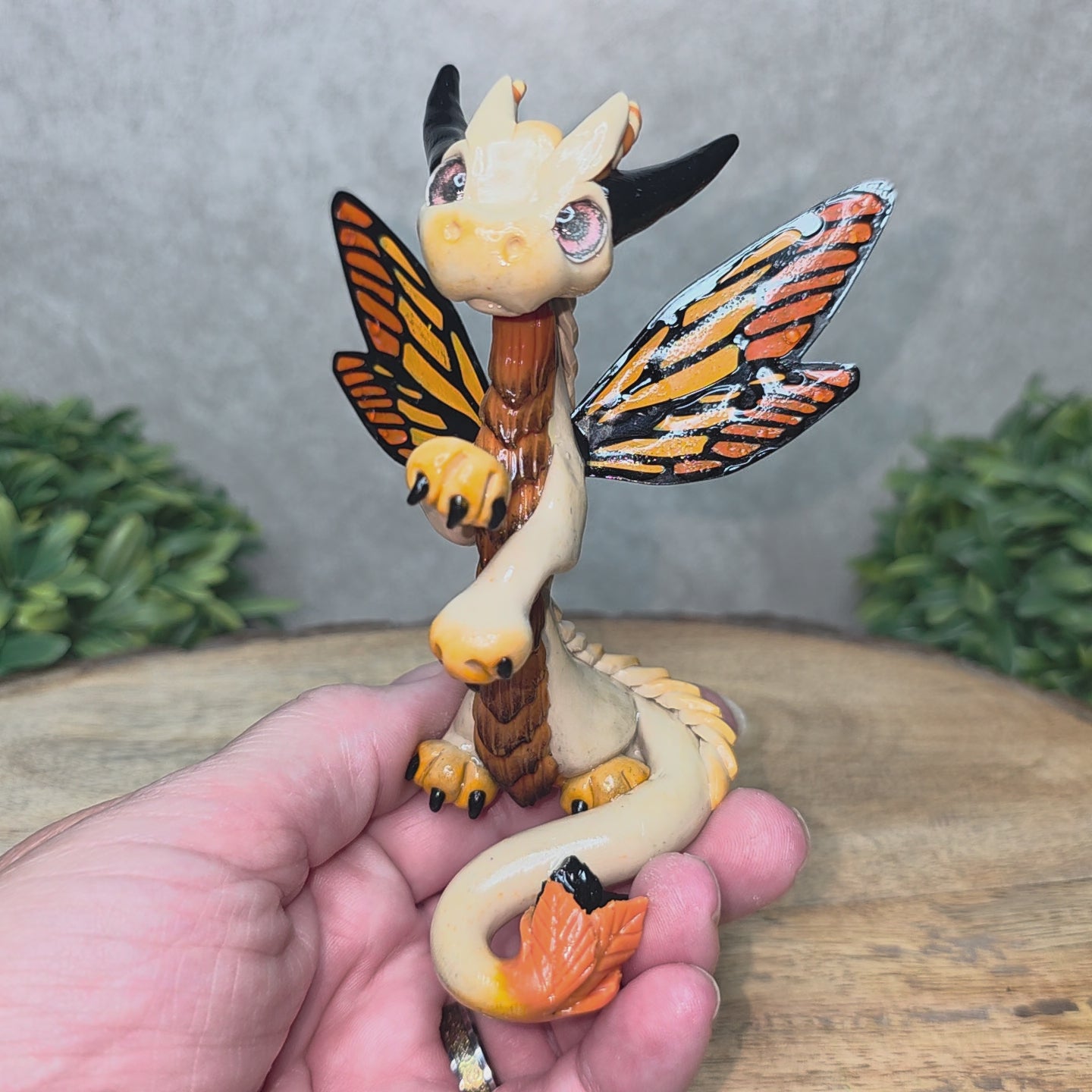 A video of a hand holding a clay dragon with butterfly wings