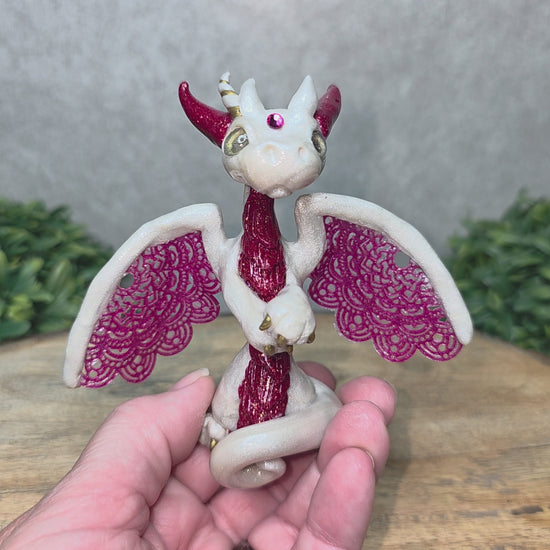 A video of A hand holding a clay dragon against a wood background with greenery