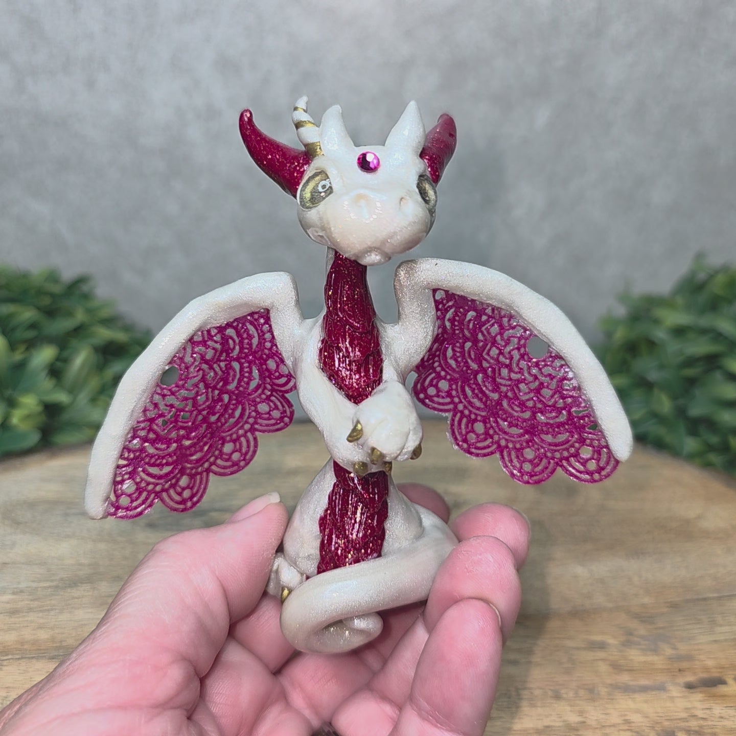 A video of A hand holding a clay dragon against a wood background with greenery