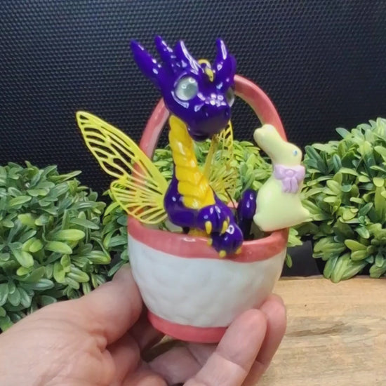 Video showing different angles of a clay fairy dragon in a ceramic Easter basket.