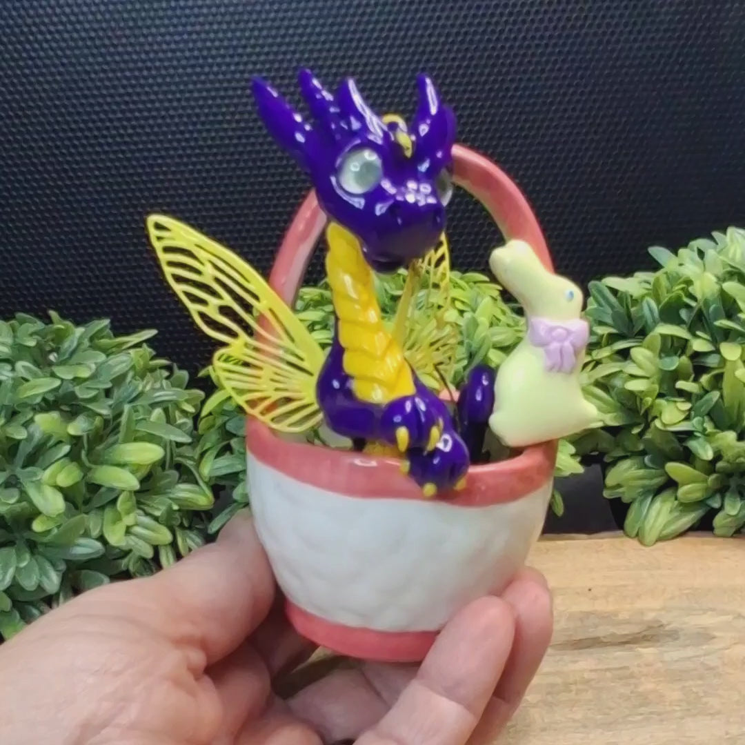 Video showing different angles of a clay fairy dragon in a ceramic Easter basket.