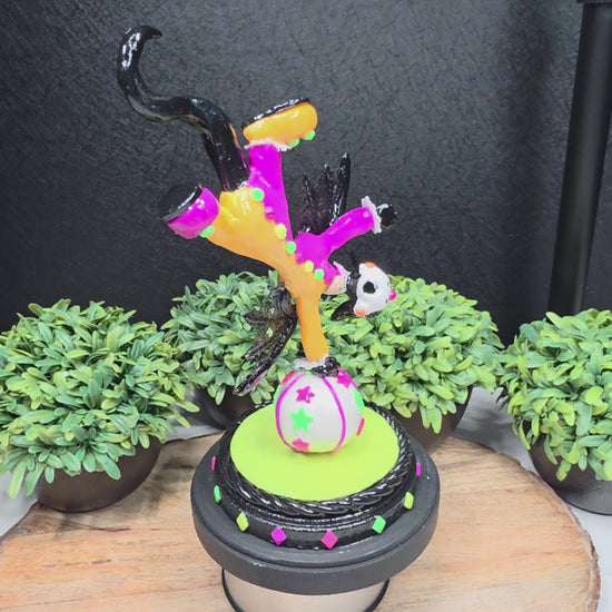 A video of a clown dragon balancing on a ball on a wood surface with greenery