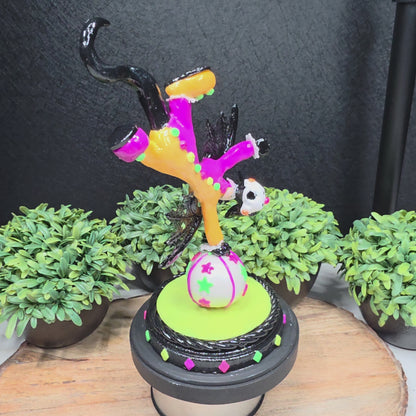 A video of a clown dragon balancing on a ball on a wood surface with greenery