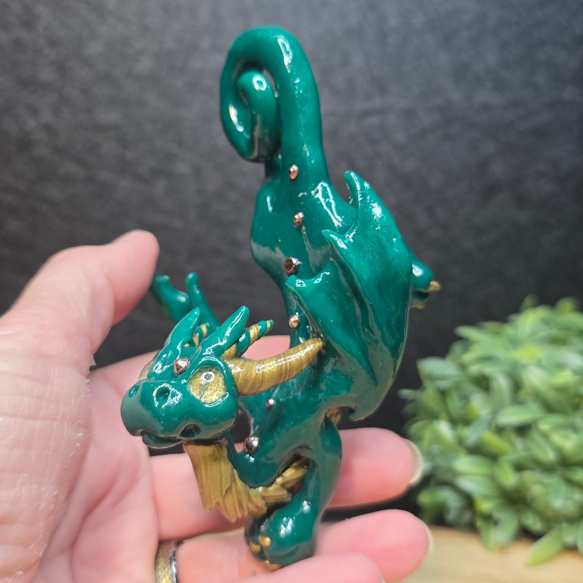 Hand holding a green and gold clay dragon