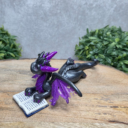 A dragon reading a book against a wood surface with greenery