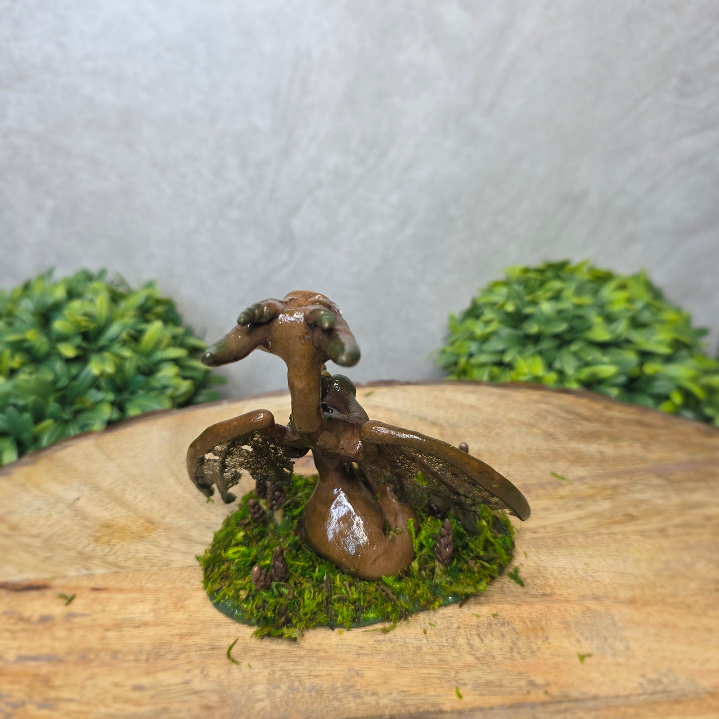 Small dragon figurine on a piece of wood with greenery in the background