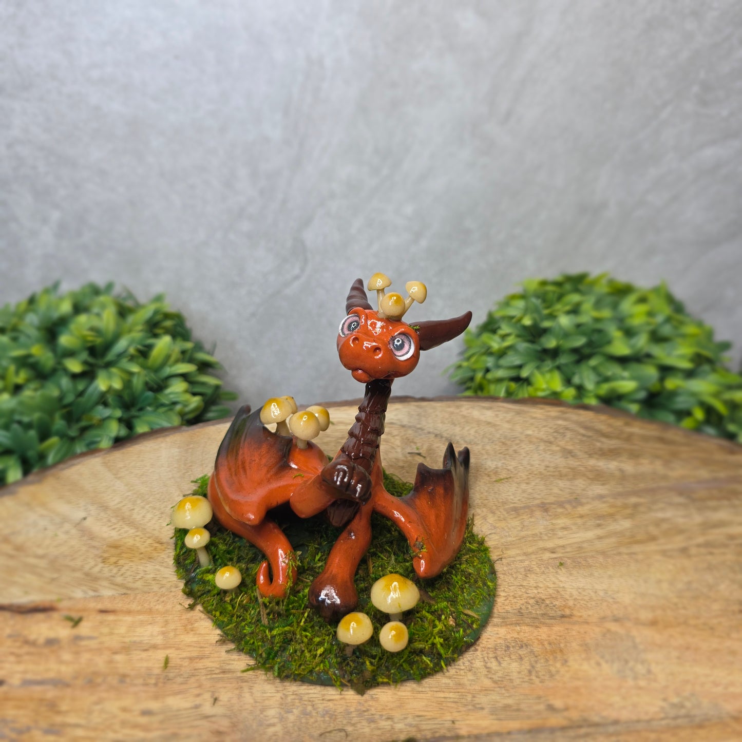 Clay dragon surrounded by mushrooms and moss against a wood background