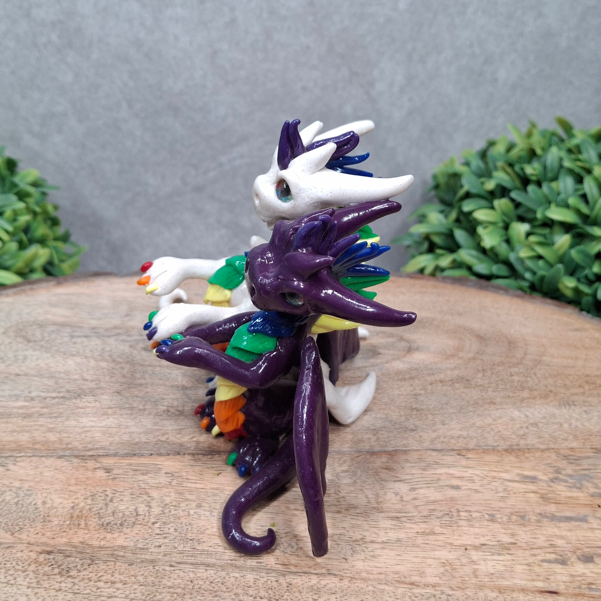 a dragon pair with rainbow accents against a wood surface with greenery
