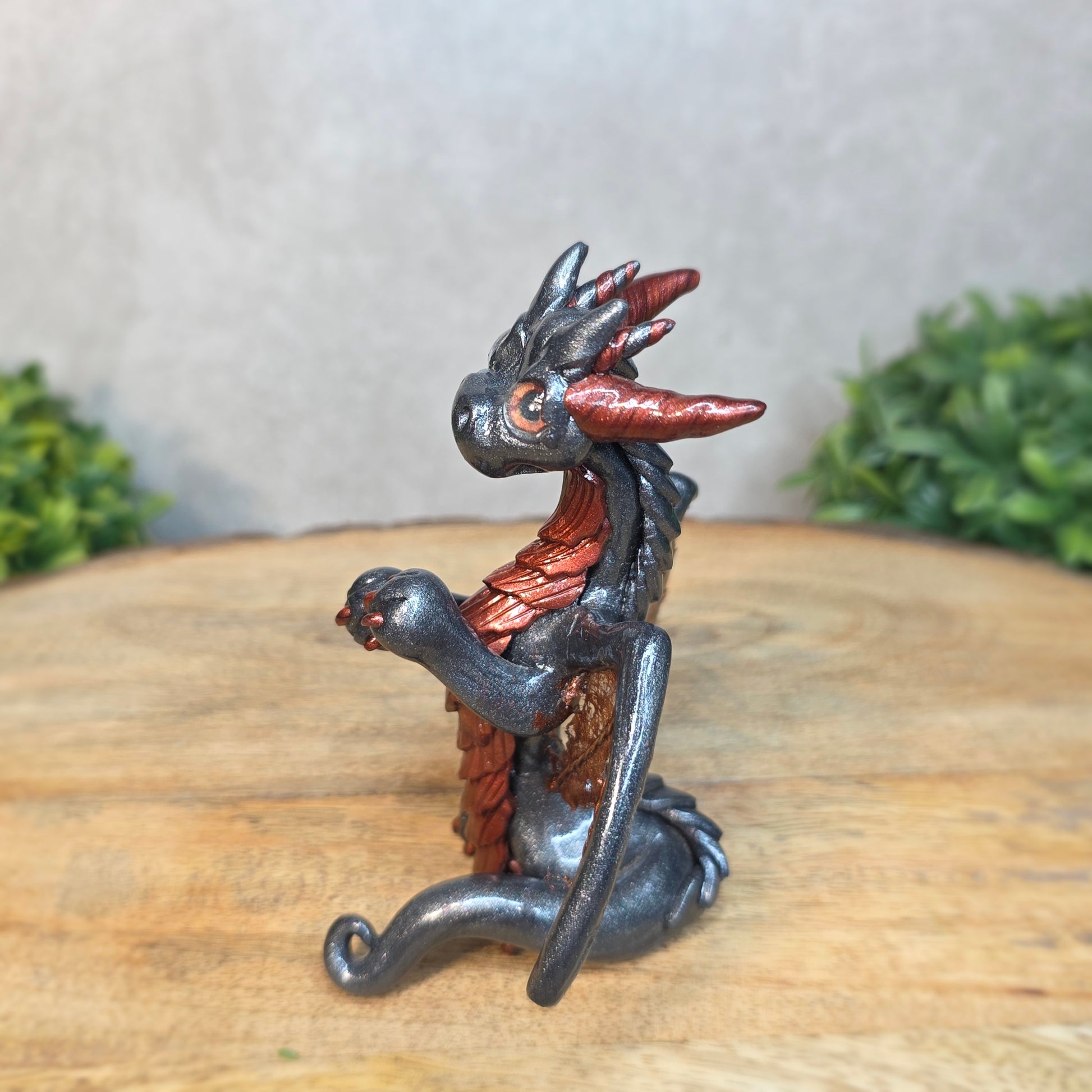 A graphite and bronze clay dragon against a blurred wood surface